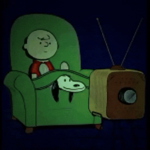charlie brown and snoopy sat in a green armchair illuminated by a tv screen